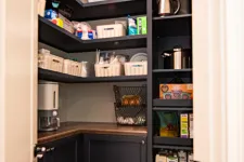Thumbnail for Organized pantry with dark shelves, storage baskets, kitchen appliances, and food items on wooden floor.