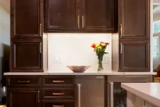 Thumbnail for Dark wooden kitchen cabinets with stainless steel appliances, white countertop, and flowers in vase on counter.