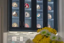Thumbnail for Dark kitchen cabinet with glass doors displaying colorful teacup sets, yellow and white flowers in foreground.