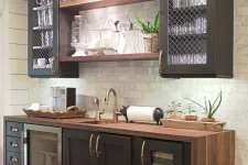 Thumbnail for Modern home bar with dark wood cabinets, wine fridge, glassware, and open shelving against white tile wall.