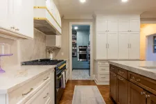 Thumbnail for Modern kitchen with white and blue cabinets, marble countertops, wooden island, and built-in oven with gas stove.