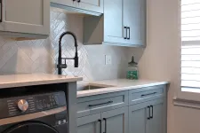 Thumbnail for Modern laundry room with gray cabinetry, black hardware, farmhouse faucet, white countertop, and dark wood floor.