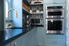 Thumbnail for Modern blue kitchen with black countertop, gold faucet, built-in stainless steel double oven, and patterned tile floor.