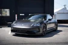 Thumbnail for Matte black Porsche Taycan electric sports car parked in front of a dark building on a sunny day
