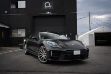 Thumbnail for Matte black luxury Porsche sports car parked outside a modern black building under cloudy sky.