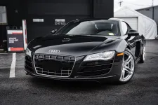 Thumbnail for Sleek black Audi sports car parked in front of a garage with a vehicle drop-off sign visible.