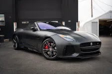 Thumbnail for Matte black Jaguar sports convertible parked outdoors with red brake calipers and sleek design details