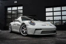 Thumbnail for White Porsche sports car parked in front of a black garage with large glass windows.