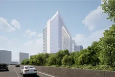 Thumbnail for Modern glass office building with signage, surrounded by greenery alongside a busy street with cars under a blue sky.