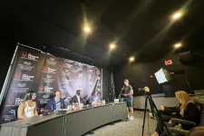 Thumbnail for Panel of four judges wearing headsets at a table with microphones under bright lights during a recording session.