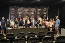 Thumbnail for Group of people posing in front of The Shrimp Tank backdrop at entrepreneurship event with a panel table and prizes.