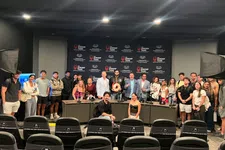 Thumbnail for Group photo of diverse people standing behind a conference table with Shrimp Tank branding in a studio setting.