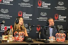 Thumbnail for Two hosts wearing headphones speaking into microphones with branded backdrop and shrimp-themed props on table