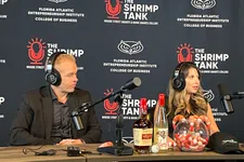 Thumbnail for Two podcasters wearing headphones speak into microphones with branded backdrop and assorted drinks on table.