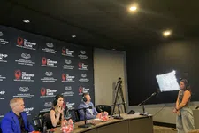 Thumbnail for Three judges sit at a panel with microphones and headphones in a podcast studio while a woman stands near a light setup.