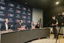 Thumbnail for Panel of four judges in a podcast studio discussing on microphones with a host standing near a camera setup.