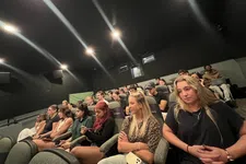 Thumbnail for Diverse group of people attentively watching a presentation or film in a dark auditorium with tiered seating.