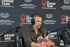 Thumbnail for Man with headphones speaking into microphone at The Shrimp Tank event with branded backdrop and shrimp bowl