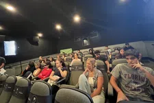 Thumbnail for Students sitting attentively in a dimly lit lecture hall with padded seats and dark walls.