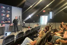Thumbnail for Two presenters speak to an audience in a small auditorium with cameras and lighting equipment set up.