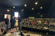 Thumbnail for Group photo of speakers and audience in a small theater-style room with microphones and recording equipment.