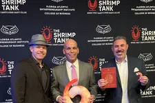 Thumbnail for Three men in suits posing at The Shrimp Tank event with shrimp props and a book against branded backdrop.