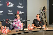 Thumbnail for Two men wearing headphones discuss business on a podcast set with The Shrimp Tank backdrop and candy jars on the table.