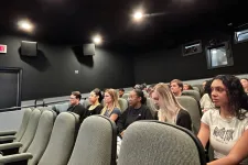 Thumbnail for A group of people attentively watching a presentation in a small, modern theater setting.