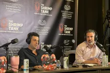 Thumbnail for Two men wearing headphones speaking into microphones on a podcast with The Shrimp Tank banner background