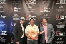 Thumbnail for Three men posing in front of a Shrimp Tank backdrop, one holding a large shrimp prop, at an entrepreneurship event.