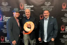 Thumbnail for Three men posing at The Shrimp Tank entrepreneurship event with shrimp-shaped trophy and branded backdrop
