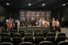 Thumbnail for Group of people posing in front of a branded backdrop with chairs in the foreground under indoor lighting.