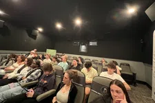 Thumbnail for A diverse group of young adults attentively watching a presentation in a dimly lit auditorium with black walls.