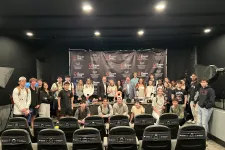 Thumbnail for Group photo of diverse young people and adults posing in front of a branded backdrop in a studio setting.
