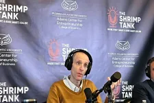 Thumbnail for Man wearing headphones speaking into a microphone at The Shrimp Tank podcast with branded backdrop and shrimp jar.