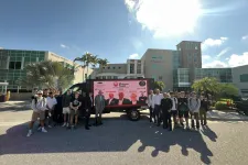 Thumbnail for Group of people posing outdoors in front of a trailer with Shrimp Tank display at a sunny campus with palm trees.