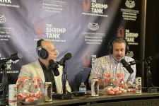 Thumbnail for Two men with headphones speaking into microphones at The Shrimp Tank podcast with shrimp and soda on the table