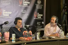 Thumbnail for Two men podcasting on The Shrimp Tank with microphones, headphones, and branded backdrop in a studio setting.