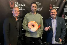 Thumbnail for Three men posing at The Shrimp Tank event with shrimp plush toys and a branded backdrop of Florida Atlantic University.