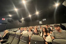 Thumbnail for Group of young adults seated in a dark auditorium or classroom, attending an event or lecture.