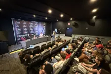 Thumbnail for Conference room with panel discussion, attendees in theater seats using laptops and cameras recording event
