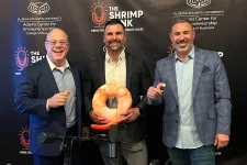 Thumbnail for Three men in suits smiling at a Shrimp Tank event with shrimp-shaped props and beverages on a table.