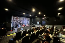 Thumbnail for a group of people sitting in a room with a stage and a large screen