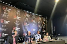 Thumbnail for Panel of four speakers with microphones in recording studio for The Shrimp Tank podcast with branded backdrop and lighting.