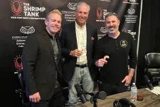 Thumbnail for Three men posing in front of The Shrimp Tank podcast backdrop with a table of podcast equipment and drinks.