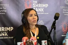 Thumbnail for Woman wearing headphones speaks into microphone at The Shrimp Tank event with promotional beverages displayed.