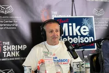 Thumbnail for Man wearing headphones speaks into microphone on podcast set with shrimp tank backdrop and campaign sign.
