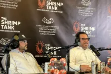 Thumbnail for Two men wearing headsets speaking into microphones during a podcast at The Shrimp Tank in front of a branded backdrop.