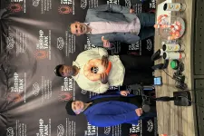 Thumbnail for Three men standing at The Shrimp Tank event with shrimp-themed products and microphone on table