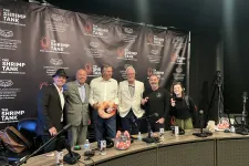 Thumbnail for Group of six people posing in front of The Shrimp Tank podcast banner in a recording studio with microphones and props.